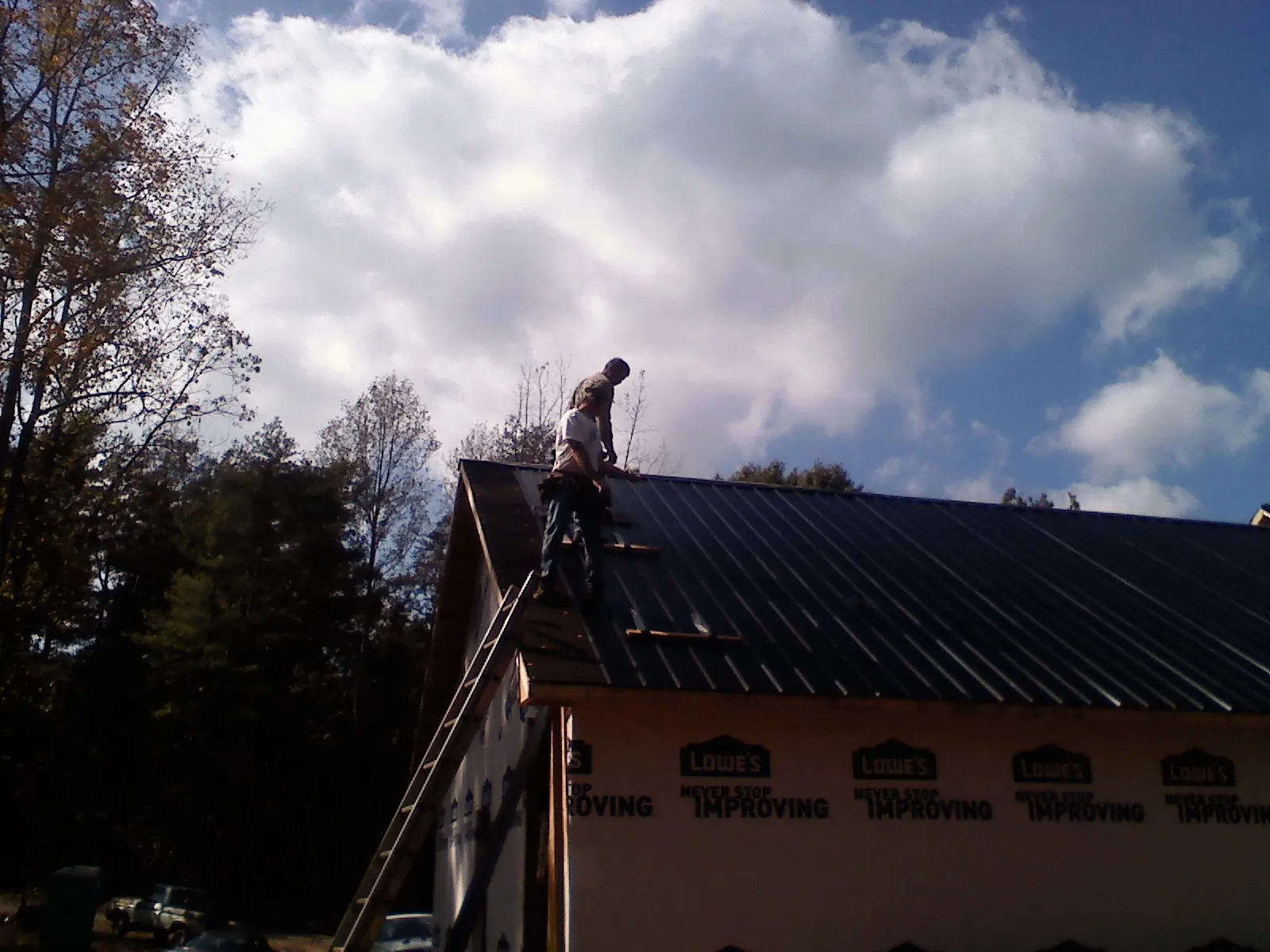 Roofer fastening dark metal panels high against a cloudy sky, from a Roof Inspection job in Ceresco